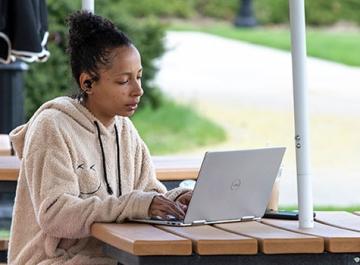 学生在校园野餐桌旁用笔记本电脑工作